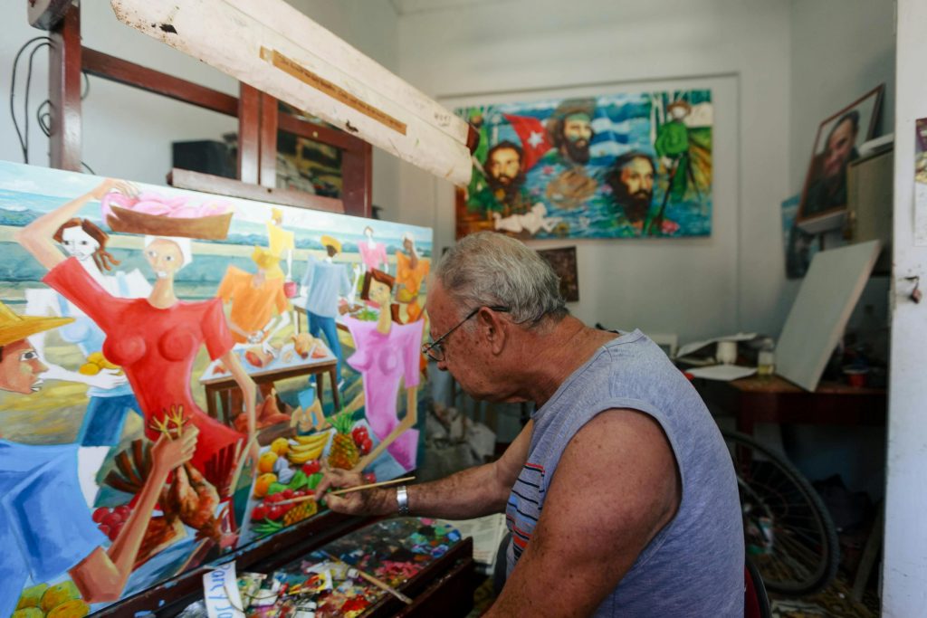 Idoso pinta tela colorida em ateliê, mostrando como a arte estimula concentração, coordenação motora e expressão emocional.