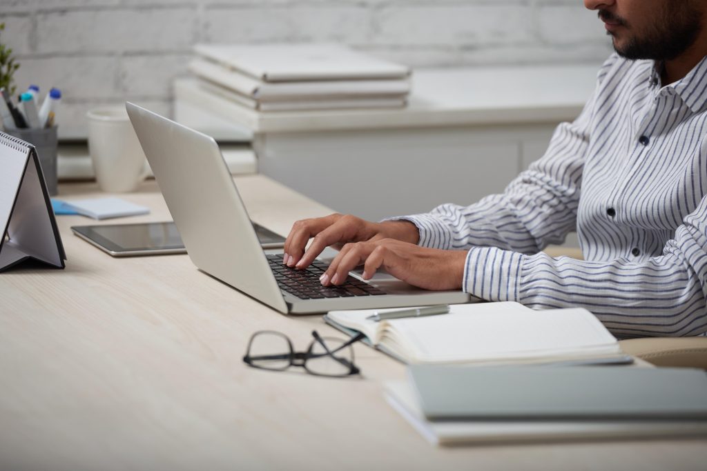 Homem estuda em notebook com caderno ao lado, representando organização para curso EAD