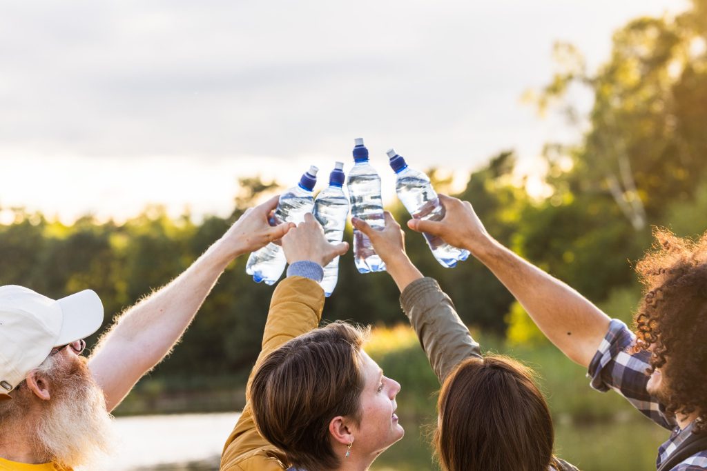 Grupo de pessoas erguendo garrafas de água em ambiente externo, simbolizando hidratação essencial para saúde intestinal