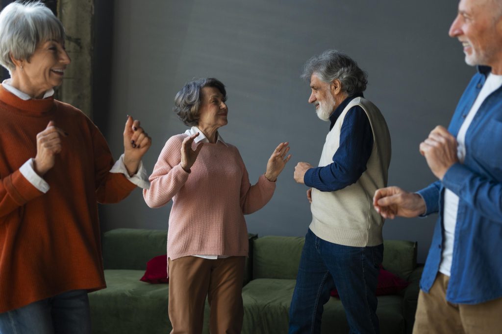 Grupo de idosos dançando juntos, mostrando como música, dança e canto promovem socialização, alegria e bem-estar.