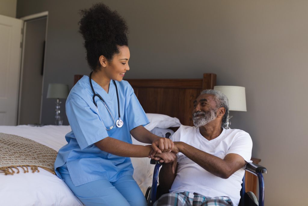 Enfermeira segura mãos de paciente idoso em cadeira de rodas, demonstrando empatia e respeito