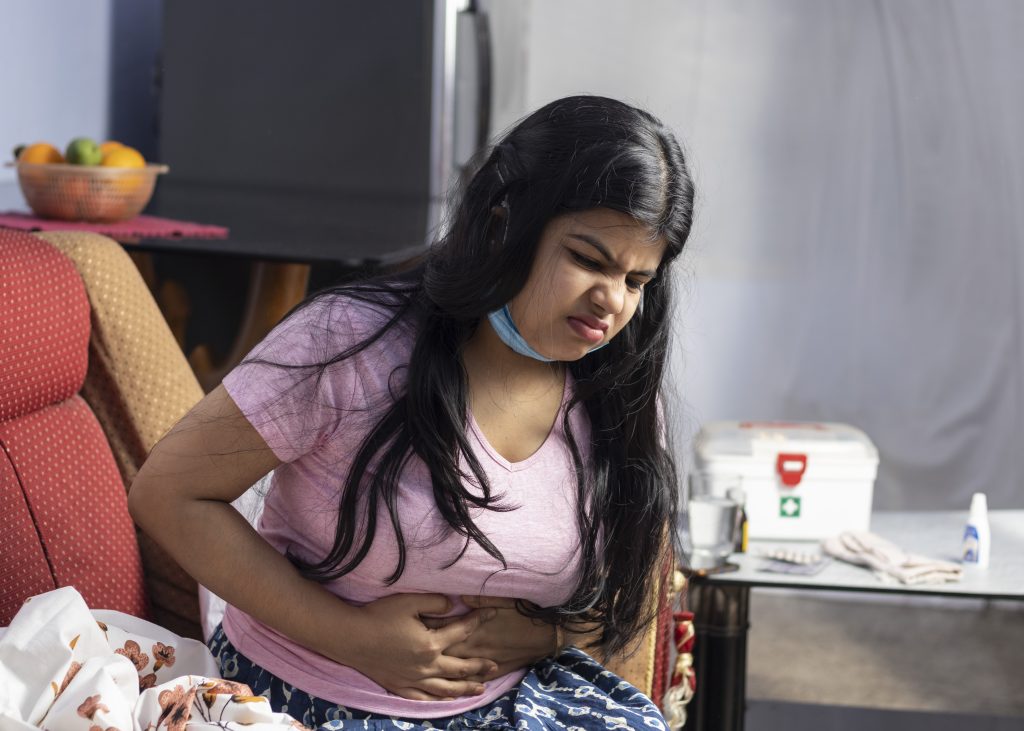 Mulher com dor abdominal segura o estômago, representando sintomas de prisão de ventre, como intestino preso e inchaço