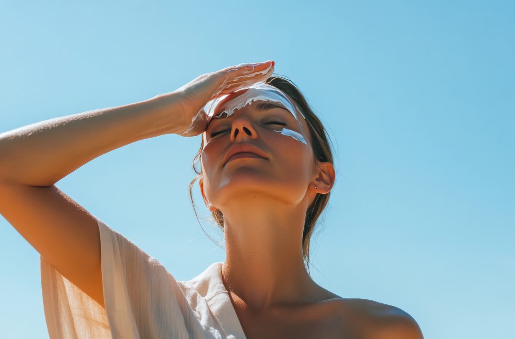 Mulher aplicando protetor solar no rosto em dia ensolarado, passo essencial para prevenir melasma e proteger a pele.