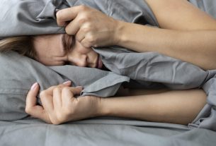 Pessoa com expressão de sofrimento, segurando a coberta, simbolizando os efeitos da apneia do sono e o impacto no descanso noturno.