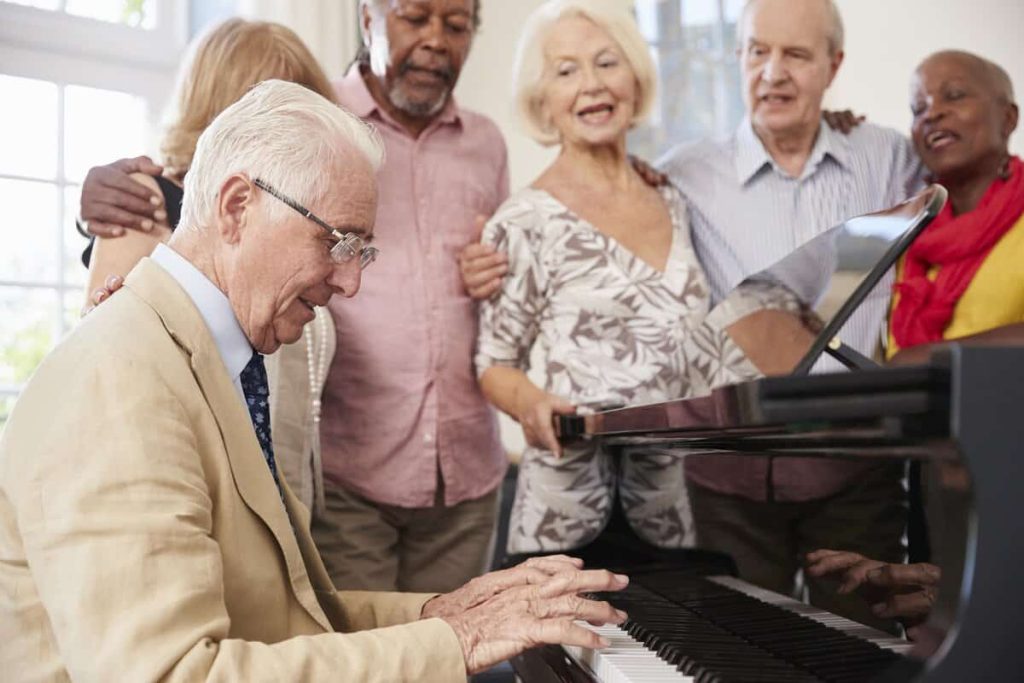 Grupo de idosos participando de musicoterapia comunitária com piano, promovendo integração social e bem-estar.