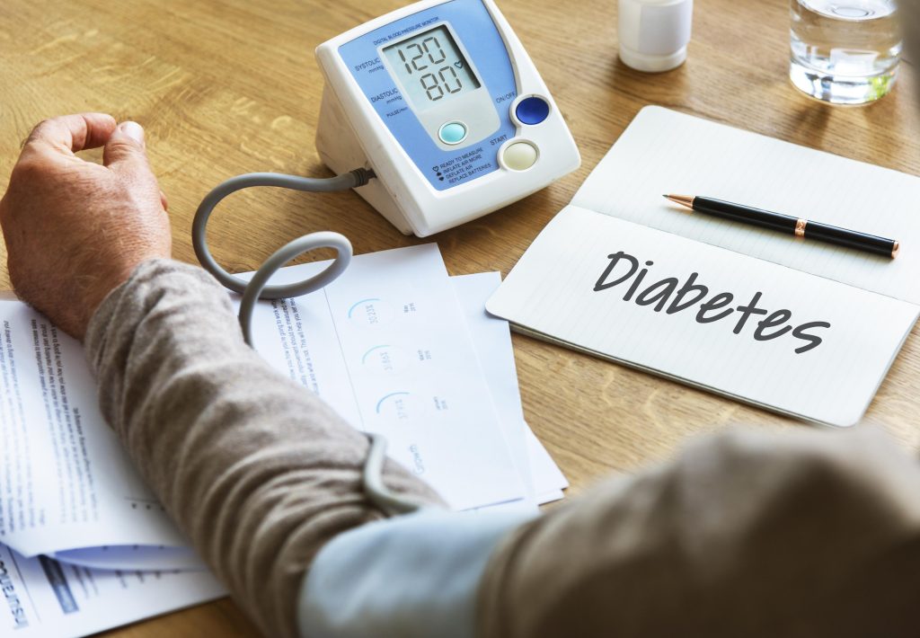 Pessoa mede pressão arterial ao lado de anotações sobre diabetes, reforçando a importância do diagnóstico precoce e controle.