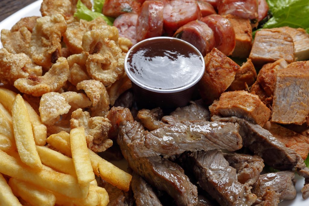 "Prato com batatas fritas, carne gordurosa e linguiça, representando alimentos fritos e ricos em gordura saturada que diabéticos devem evitar para controlar os níveis de glicose.