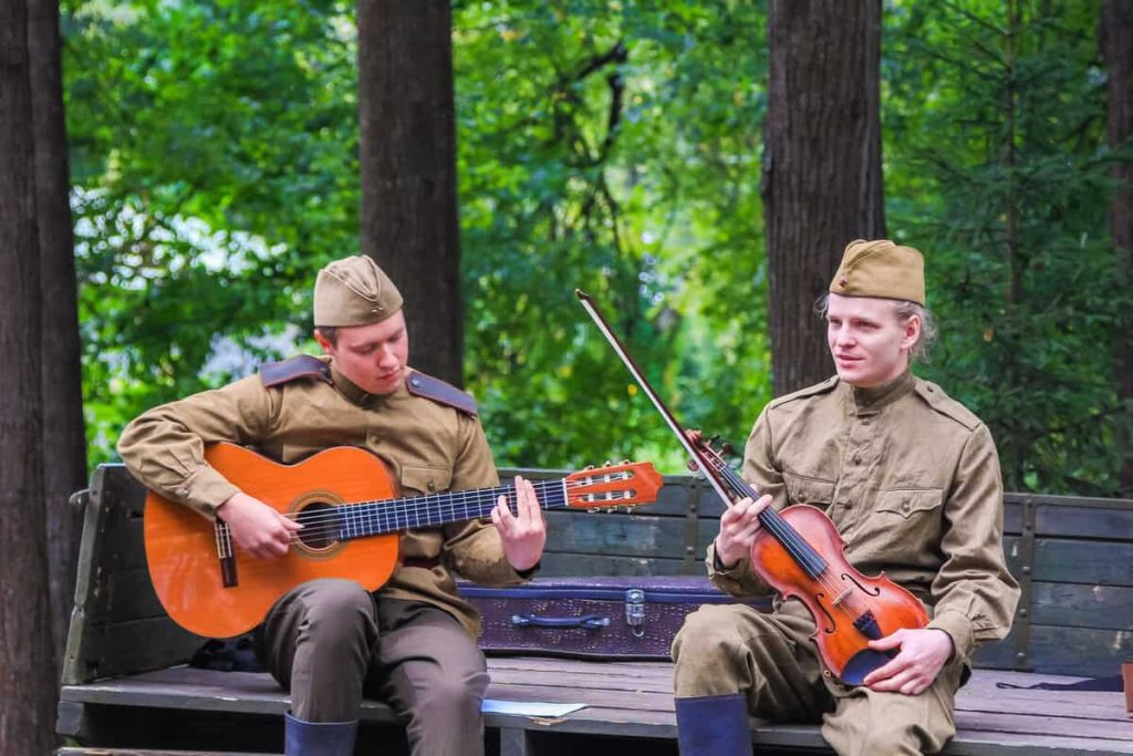 Soldados tocam violão e violino durante a guerra, retratando o uso da música como apoio terapêutico na recuperação emocional.