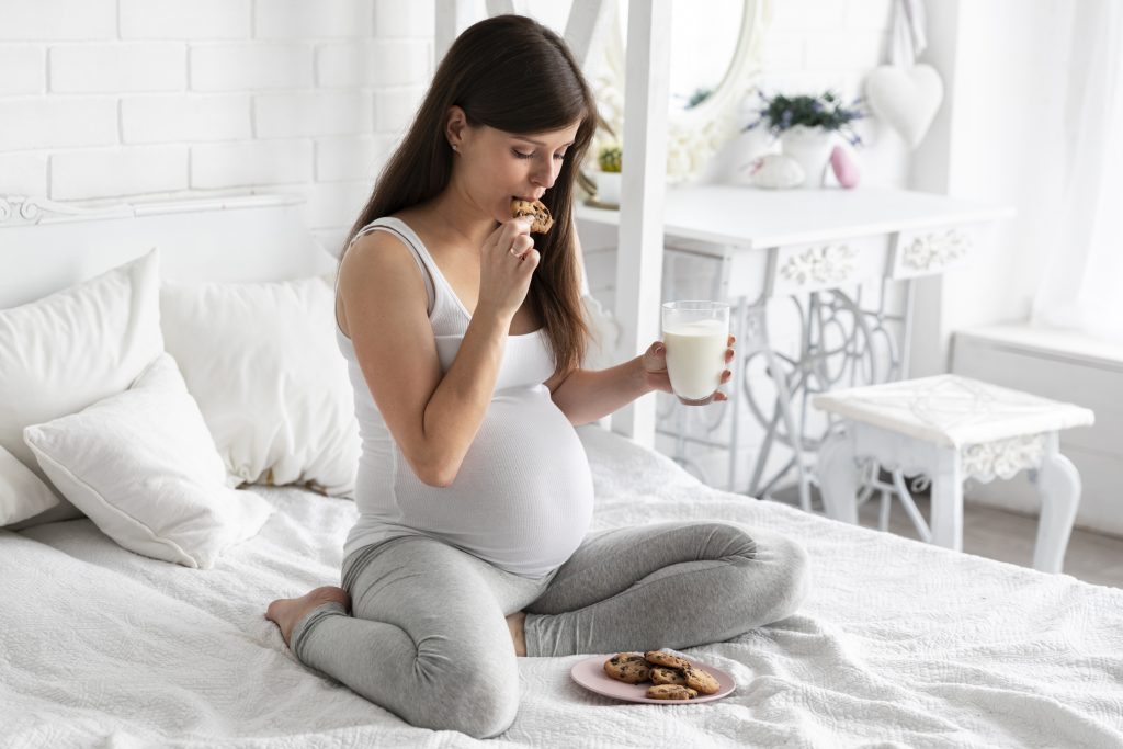 Gestante sentada na cama, segurando leite e biscoitos, representando sintomas da anemia na gravidez