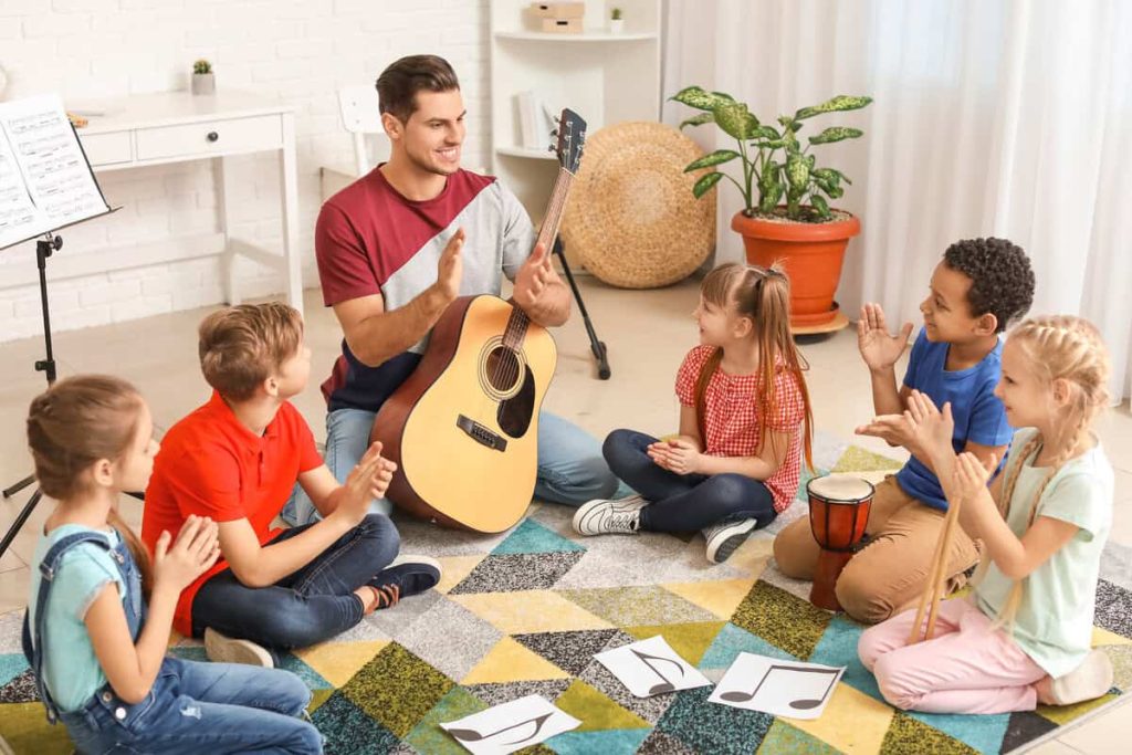 Crianças participam de sessão de musicoterapia em grupo com violão e percussão, promovendo bem-estar, socialização e aprendizado.
