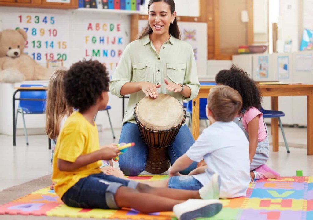 Profissional de saúde conduz sessão de musicoterapia com crianças em ambiente escolar, estimulando interação e aprendizado.