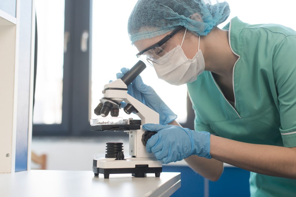 Cientista em laboratório manuseia pipeta e placa de Petri durante pesquisa farmacológica.