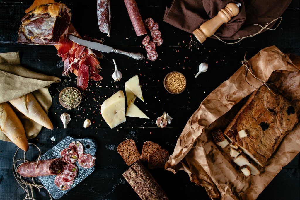 Mesa com queijos, embutidos e pães, alimentos que podem desencadear crises de enxaqueca