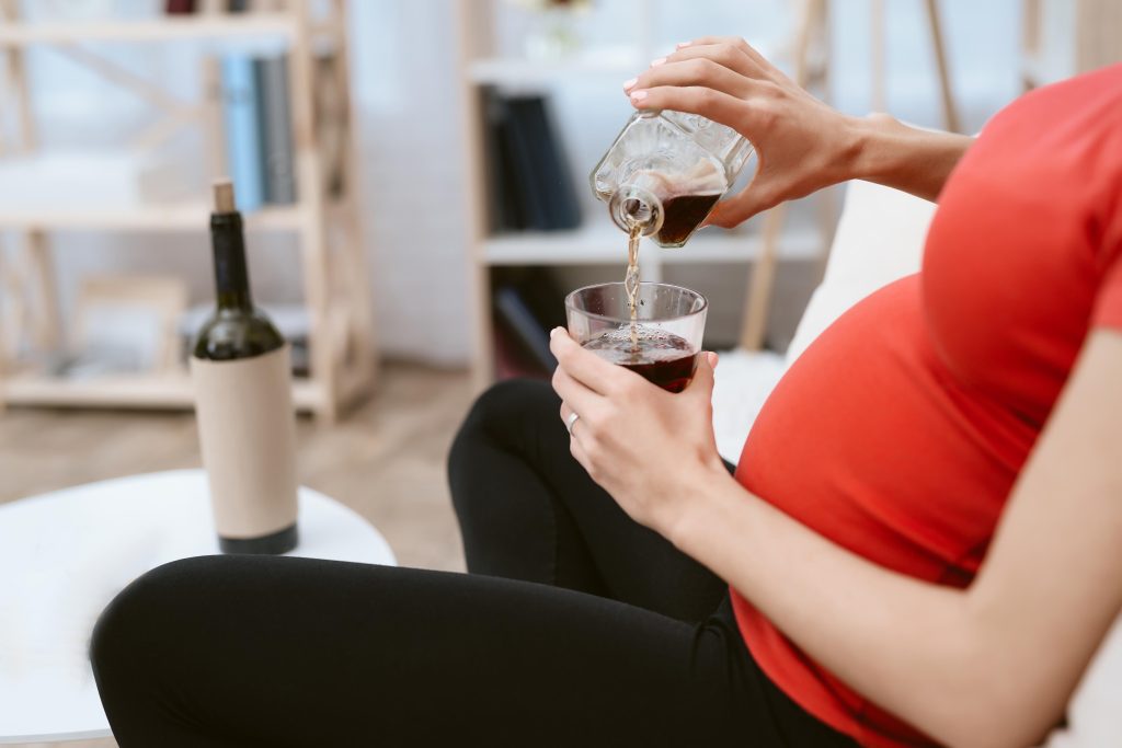 Gestante segura copo com bebida alcoólica, ilustrando risco de perda gestacional